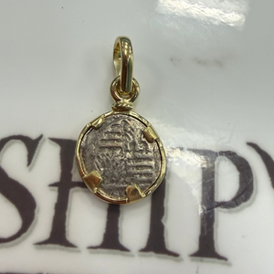 A small gold pendant charm shaped like an antique coin with a loop at the top, resting on a white surface with dark printed letters.