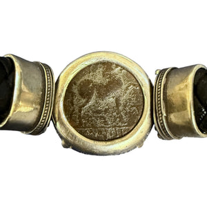 A close-up of a vintage-style metal bracelet or belt featuring a central oval medallion with an embossed animal motif, flanked by two cylindrical links with decorative ridges, on a plain white background.