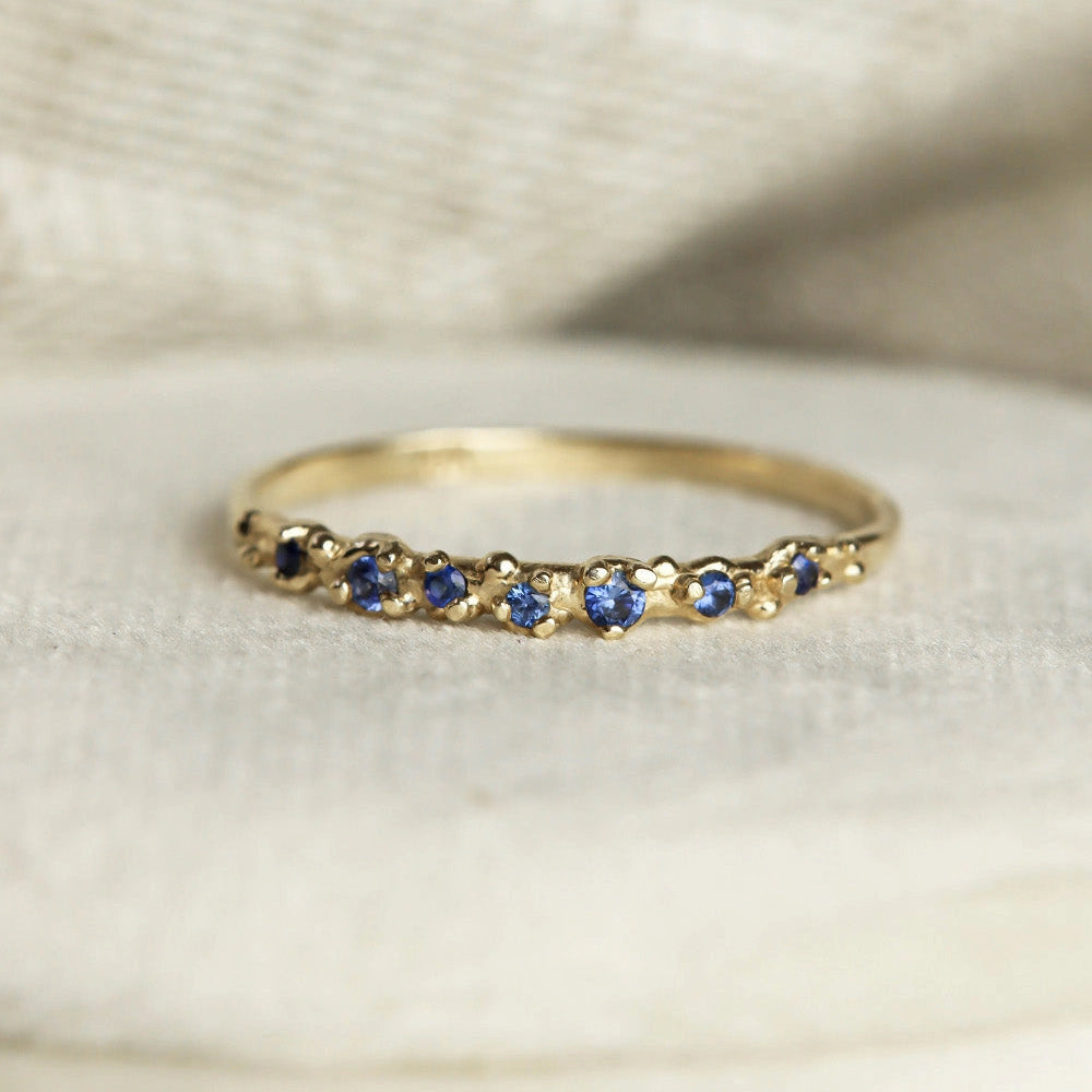 Gold ring with blue gemstones on a textured beige background