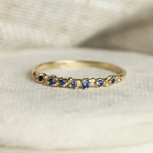Gold ring with blue gemstones on a textured beige background